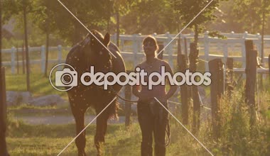 Ağır çekim Dof: çarpıcı at alanından corrals Altın ışık akşam ahıra arasında önde gelen kız. Genç kadına muhteşem yaz gün batımında pastoral çiftlik evi tatilde çalışma