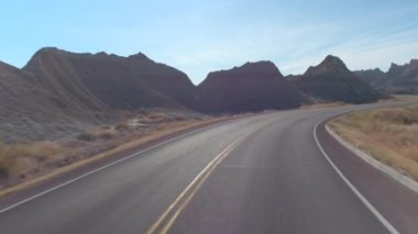 FPV: pitoresk Badlands yatay, kayalık kumtaşı oluşumları üzerinden kıvrıla kıvrıla boş yol boyunca sürüş. Güney Dakota'daki Badlands Çölü seyahat. Yolculuk boyunca Amerika Birleşik Devletleri.
