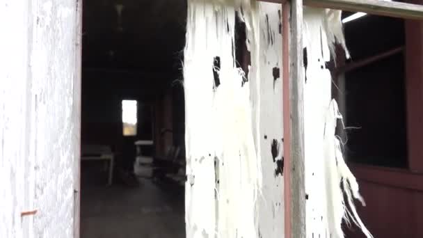 透过一个被毁的旧腐烂的木舱的破碎的窗户 可怕的白色窗帘在风中拍打 可怕的教室 学校甲板被破坏 在废弃的破败的房子里 — 图库视频影像