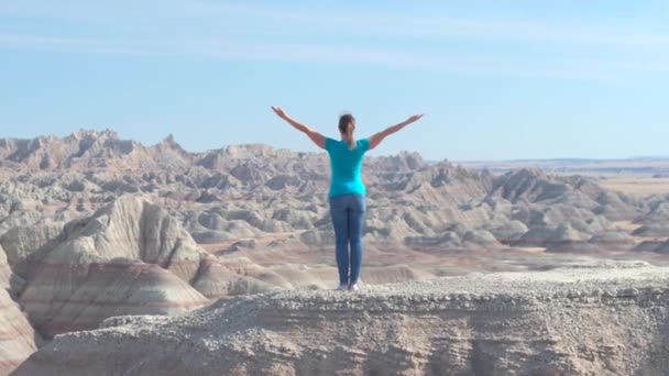 スローモーション幸せ女性ハイカーが晴れた空を楽しんで リラックスへ上がる彼女の腕と砂岩バッドランズ国立公園の山の上に立っています 旅行者探索のバッドランズ国立公園の荒野 — ストック動画
