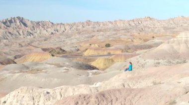 Badlands Ulusal Parkı güneşli günde Güney Dakota'da, ABD çarpıcı manzaranın kayalık dağ yamacında oturan genç kadın seyahat etmek. Mutlu kız kumtaşı dağ çöl vahşi keşfetmek