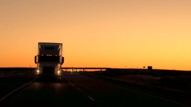 Yakın: doğal ülke karayolu boyunca yük konteyner yarı römork kamyon sürme. Yoğun trafik dramatik turuncu gökyüzü ile güzel altın ışık alacakaranlıkta karayolunda. Araçlarda yol yolculuk yolculuk