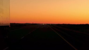 Yakın: Yük konteyner yarı römork kamyon Great Plains içinde birden çok şeritli ülke otoyol boyunca güneş battıktan sonra sürüş mal taşıma ön görünümü. ABD genelinde seyahat kamyon sollama