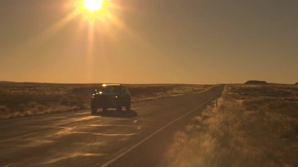 空中は クローズ アップ フィールドの広大な牧草地に囲まれた荒涼とした田園地帯を渡って黒の Suv 車の上を飛んでください 素晴らしい黄金光日当たりのよい砂漠の空高速道路に沿って運転敢行の人々 — ストック動画