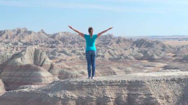 スローモーション幸せ女性ハイカーが晴れた空を楽しんで リラックスへ上がる彼女の腕と砂岩バッドランズ国立公園の山の上に立っています 旅行者探索のバッドランズ国立公園の荒野 — ストック動画
