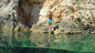 Split sualtı, ağır çekim, çiftlikteki atlama yakın kadar atletik genç adam bir kaba kayalık deniz cliff waterdrops etrafında sıçramasına kristal berraklığında Akdeniz kapalı. Sahil, aktif tatiller