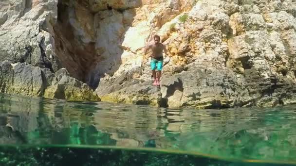 分割水中 スローモーション 頭から跳躍運動を近くの若い男大まかな岩海崖から透き通った地中海に周りの水滴を飛散します 海辺でアクティブな休日 — ストック動画