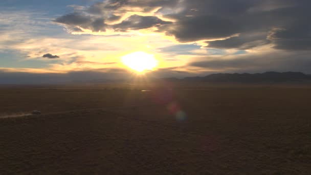 航空写真 ドラマチックな日没で砂漠の谷を通って黒い Suv 車の上を飛んでください 風が吹いてダート トラックのダスト粒子を発生します ロッキー山脈の道旅の人々 — ストック動画