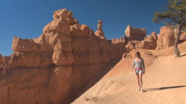 Boş yolda yürüyen genç kadın gezgin kumtaşı Hudu oluşumları Bryce Canyon Milli Parkı'nda güneşli Utah keşfetmek. Genç kadın turist tozlu yolun Bryce Canyon ABD hiking