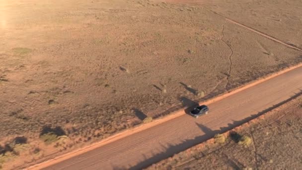 航空写真 Suv 車の晴れた朝にユタ州の空のほこりっぽい道トラフ乾燥草原砂漠の谷に沿って運転 黄金の夕日でキャピトル リーフにストレート土ルートを走るジープの上飛行 — ストック動画