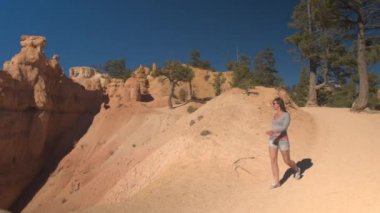 Kumtaşı Hudu oluşumları bakış açısı Bryce Canyon Milli Parkı'nda Utah, hayran boş yolda yürüyen genç kadın uzun yürüyüşe çıkan kimse. Genç kadın turist tozlu yolun Bryce Canyon ABD hiking