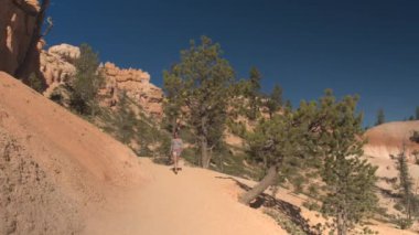 Kumtaşı Hudu oluşumları Bryce Canyon Milli Parkı'nda güneşli Utah keşfetmek dolambaçlı yol boyunca yürüyüş genç kadın uzun yürüyüşe çıkan kimse. Genç kadın turist tozlu yolun Bryce Canyon ABD hiking