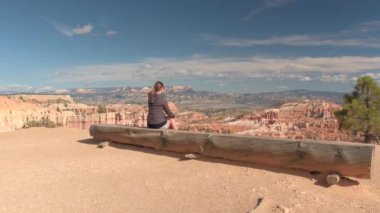 Mutlu yürüyüşçü Bryce Canyon Amfitiyatro çarpıcı bir görünüm izlerken ahşap bankta oturan. Bryce Canyon Milli Parkı'nda kumtaşı hoodoos ve kayalık sütunlar bakan pitoresk bakış açısı.