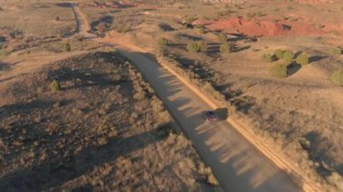 Anteni: boş tozlu yol yalak kuru çayır çöl Vadisi Utah güneşli sabahı araba siyah Suv araba. Uçan yukarıda altın günbatımında Capitol resif düz toprak yolu üzerinde seyahat jeep