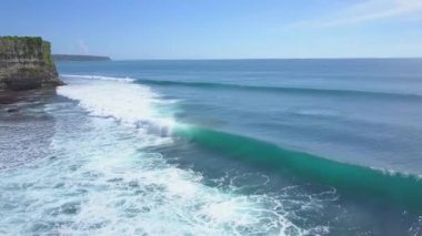 Anteni: köpüklü dalgalar güneşli Bali Adası uzun boylu cliffy duvara güzel kayalık Plajı kırma yıkama. Okyanus su yüzeyi üzerinde yükselen kaya zor. Ufka uzanan masmavi deniz