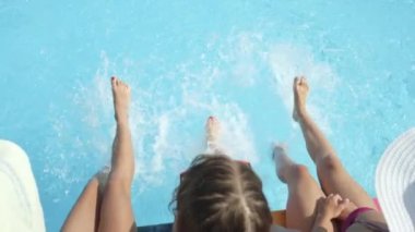 Sıcak güneşli günde ayakları ile su sıçramasına havuzu kenarında oturan ağır çekim yakın kadar Lens Flare üç tanınmaz neşeli kız. Su sıçramasına yaz tatilde üç oynak genç kadın