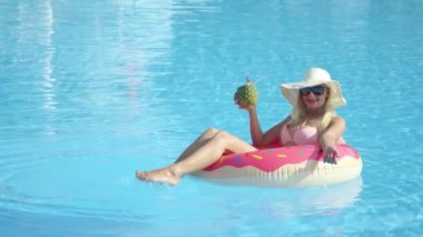 Ananas içki yudumlarken ve şişme pembe halka float rahatlatıcı ağır çekim yakın kadar mutlu sarışın kız. Yaz tatili havuzu pembe floatie üzerinde kokteyl içme zevk Bikini genç kadın