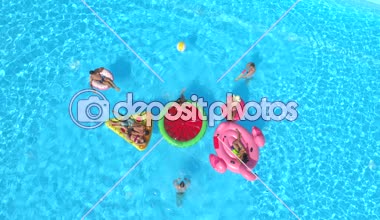 Hava: neşeli arkadaşları su havuz partisinde renkli floaties fight. Oynak çocuklar ve kız alma selfies şişme pizza, halka, flamingo ve karpuz yüzen üzerinde ve su sıçramasına