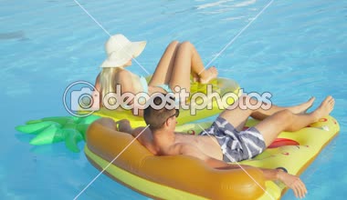 Yakın: döşeme ve pizza ve ananas floaties havuzunda rahatlatıcı genç çift uygun. Kız ve erkek arkadaşı yaz tatile eğlenceli renkli su içerisinde yüzen yüzen zevk sıcak güneşli bir gün