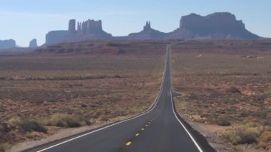 İlk kişi görünümü ikonik Monument Valley landmark Utah ABD doğru düz boş bir yol boyunca sürüş. Monument Valley çöl yatay olarak sarı lekeler ile yeni otoyol yolda seyahat Pov