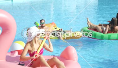 Ağır çekim yakın kadar mutlu gülümseyen öğrenciler bahar havuz partisinde renkli floaties fight su tabancası var. Şişme flamingo pizza karpuz ve halka eğlenceli neşeli genç insanların yok