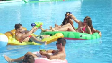 Ağır çekim yakın çekim: Oynak gülümseyen yaz aylarında havuz partisinde renkli floaties üzerinde zevk arkadaş grubu. Neşeli gençler eğleniyor şişme pizza, karpuz ve halka