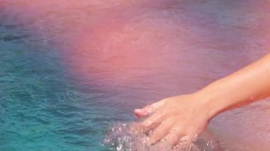 Ağır çekim yakın kadar Lens Flare detayını sürükleyerek ve berrak deniz su yüzey sıçramasına köpüklü waterdrops eline sürgülü genç kadın. Kız yapma çevrelerin okyanusta oynamaktan