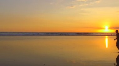 Ağır çekim, Close Up: yumuşak kumlu plaj boyunca çıplak ayakla çalışan genç adam. Okyanus dalgaları Waterdrops dramatik Altın ışık günbatımında sıçramasına. Adam gece karanlığında deniz kıyısı koşu yaz giysileri