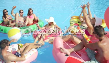 Ağır çekim yakın kadar mutlu gülümseyen öğrenciler bahar havuz partisinde renkli floaties fight su tabancası var. Şişme flamingo pizza karpuz ve halka eğlenceli neşeli genç insanların yok