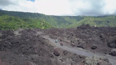 Anten, Close Up: Çift overgrown Mount Batur vulcano jant doğru kaba lav kayalık arazi boyunca toprak yolda scooter sürüş. Volkanik krater üzerinde turistik tatil için traveing motosiklet turistler