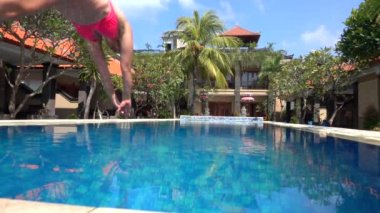 Slow Motion Close: Yaz tatilinde genç bir kadın sıcak güneşli bir günde serinlemek için önce mavi havuz suyuna atlıyor. Pembe bikinili kız boş lüks otellerde temiz havuza dalıyor.