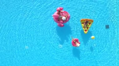 Aerial Top Down Fit kızları ve mayolu adam şişme pizza, çörek ve flamingo üzerinde yüzüyorlar. Arkadaşların tatilde pembe flamingo, çörek ve pizza yiyor.
