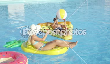 Yakın plan: formda genç bir çift pizza ve ananas şamandıraları uzatıyorlar ve bilardoda topla oynuyorlar. Kız arkadaş ve erkek arkadaş, sıcak ve güneşli bir günde eğlenceli renkli yüzgeçlerde yaz tatilinin tadını çıkarıyorlar.