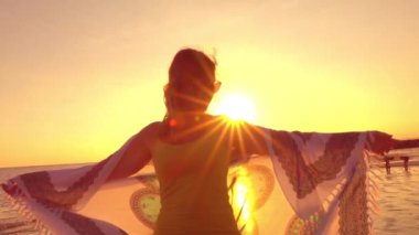 Yakın kadar ağır çekim, siluet: Çekici genç kadın rüya gibi Bali adasında muhteşem altın ışık batımında güzel rüzgarlı yaz akşamı sallayarak eşarp tutan plajda durup gözlüklü