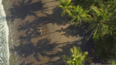 Hava: sörf onun elinde tutan ve okyanus dalgalarının sıçramasına boyunca güzel kum plajındaki volkanik yürüme çekici kas adam yukarıda uçan. Güneşli Bali etkin yaz tatilde genç adam