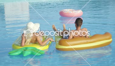 Yakın: Tanınmayan genç çift pizza ve ananas floaties havuzu üzerinde rahatlatıcı. Kız ve erkek arkadaşı döşeme yaz tatilde renkli yüzen eğlenceli ve sıcak güneşli günde ellerimi