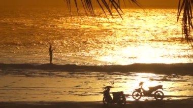 : Ağır çekim siluet tropikal balık okyanustan olta kullanarak yakalamak dalgalanan deniz kenarında rocky resif üzerinde duran eğlence balıkçı. Rüya gibi kanca ile günbatımı Balıkçılık Bali turist