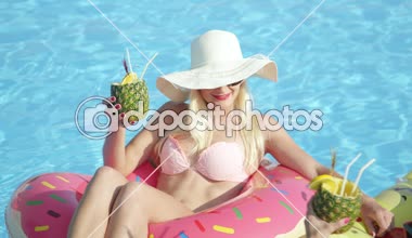 Ağır çekim yakın çekim: eğlenceye döşeme iki gülümseyen kız arkadaşım renkli floaties, yaz tatili alkollü içecekler içme. Kokteyl yudumlarken, şişme pizza ve pembe çörek üzerinde rahatlatıcı genç kadınlar