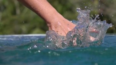 Ağır çekim yakın kadar detayını sürükleyerek ve eline su yüzey sıçramasına köpüklü waterdrops sonsuzluk havuzunda sürgülü genç kadın. Tropik adada rahatlatıcı yaz tatillerini üzerinde kız