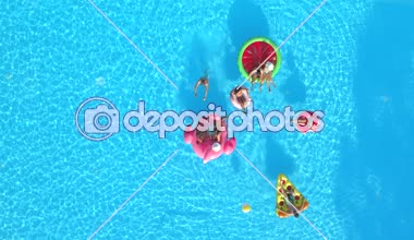 Hava aşağı üst: mutlu kızlar ve çocuklar floaties havuzu üzerinde topu ile oynamıyor. Yaz tatili şişme ananas, pizza, flamingo, karpuz ve halka yüzen zevk neşeli gülümseyen arkadaşlar