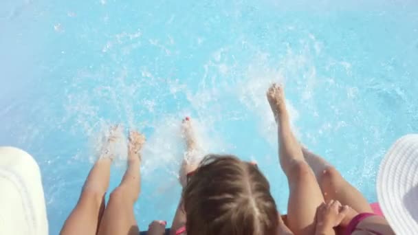 Lassú mozgás szoros fel objektív Flare három felismerhetetlen vidám lány ül a medence szélén, fröccsenő víz a lábukkal, a forró napsütésben. Három játékos fiatal nők, a fröccsenő víz nyaralás