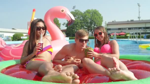慢动作特写 年轻女孩和小伙子们在有趣的充气西瓜和火烈鸟漂浮物上喝着含酒精的鸡尾酒 快乐的朋友们在游泳池里享受着五彩缤纷的夏天 — 图库视频影像