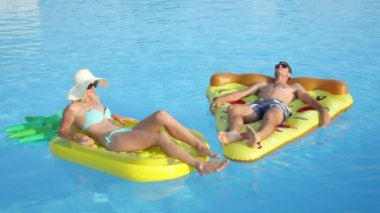 Yakın: döşeme ve pizza ve ananas floaties havuzunda rahatlatıcı genç çift uygun. Kız ve erkek arkadaşı yaz tatile eğlenceli renkli su içerisinde yüzen yüzen zevk sıcak güneşli bir gün