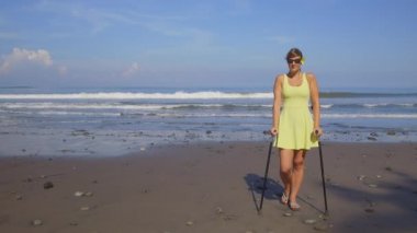 Yakın: koltuk değneği ile yaz plaj tatil seyahat kaygısız güçlü bağımsız kadın. Gülümseyen kız iyi sağlık sigortası olan hiçbir endişe ile tatil zevk kumlu kıyısında ayakta