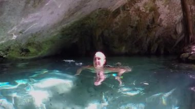 Yaklaş, Ağır Çekim: Güzel genç bir kadın yaz güneşiyle aydınlatılmış Grand Cenote mağarasında tatlı nehir suyunda yüzüyor. Turist kız banyo yapıyor ve yeraltı karst mağaralarını keşfediyor.