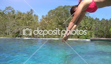 Ağır çekim yakın Lens Flare Up: Pembe bikini tekniklerle su sıçramasına içine atlama genç kadın sonsuzluk havuzunda bırakır. Akasya kız zevk yaz tatil palmiye ağacı orman resort güneşli Bali