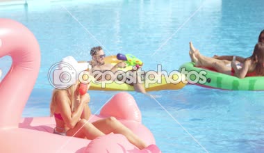 Ağır çekim yakın kadar mutlu gülümseyen öğrenciler bahar havuz partisinde renkli floaties fight su tabancası var. Şişme flamingo pizza karpuz ve halka eğlenceli neşeli genç insanların yok