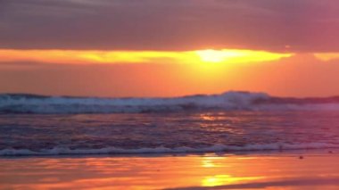 Ağır çekim yakın Up, Lens Flare: ıslak tropikal kumsalı muhteşem pembe batımında romantik yaz akşamı Bali adasında okyanus dalgalar yıkama. Kırmızı ve turuncu güneş doğarken sıçramasına dalgalanma dalgalar deniz