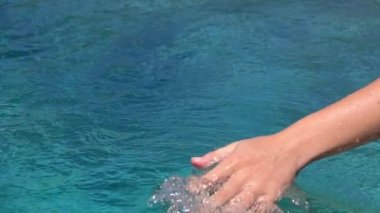 Elini su yüzeyinde sürükleyip kayan, su damlaları sıçratan ve kristal berrak denizde dalgalar yaratan genç bir kadının ayrıntıları. Okyanus suyuyla oynayan kız daireler çiziyor