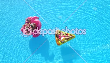 Havadan Aşağı: Genç formalı kızlar ve mayo giyen adam şişme pizza ve suyun üzerinde yüzen pembe flamingo üzerinde yatıyor. Mutlu arkadaşlar tatilde pembe flamingoda dinleniyor ve pizza havuzda yüzüyor.